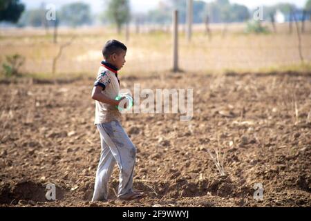 Young indian boy carrying a plastic bottle of water to father working in the field sitting on gunny bag, sacks of wheat filled after harvest in the Stock Photo