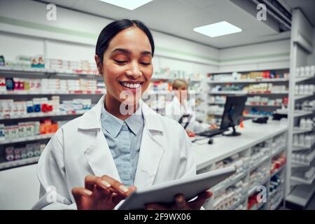 Happy woman working in medical store wearing labcoat using digital tablet Stock Photo