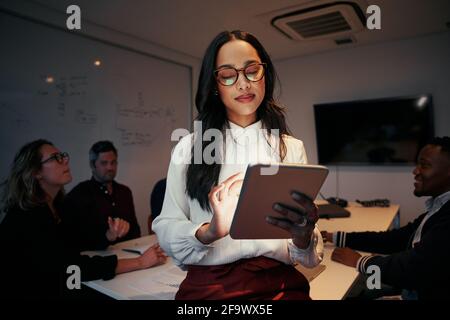 Portrait of a businesswoman using digital tablet with her team sitting at desk in meeting room Stock Photo