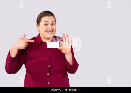 Overweight positive obese woman showing blank business card, empty credit card on grey background. Close up with side space for ad and publicity Stock Photo