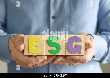 Man holds wooden cube blocks with abbreviation ESG, concept of checking company for business environmental friendliness for reliable investment. Envir Stock Photo