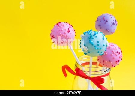 Different cake pops in the glass jar on the yellow background. Copy space. Closeup. Stock Photo