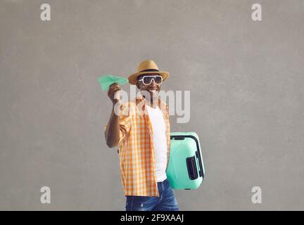 Happy smiling black tourist holding suitcase and paper plane isolated on gray background Stock Photo