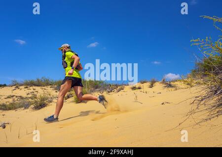 Athlete running off-road in the wild. A man in shorts and a T-shirt is running through the sandy wilderness. Stock Photo