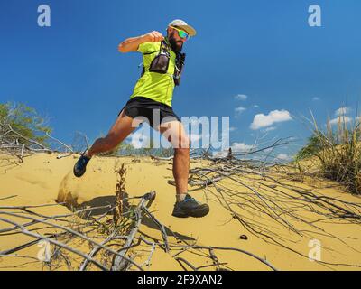 Athlete runs along the sandy desert. Desert trail running. A man in shorts and a T-shirt is running through the sandy wilderness. Stock Photo
