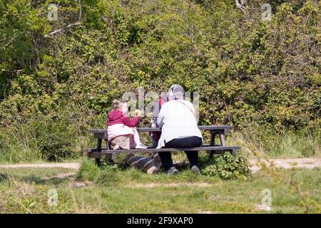 04-19-2021 Portsmouth, Hampshire, UK Grandparents sitting with their grandchild on a picnic bench in the sun eating Stock Photo