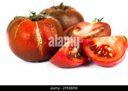 Dewy dark tomato, one with nice cracked skin, whole and halved, isolated on white background. Closeup. Stock Photo