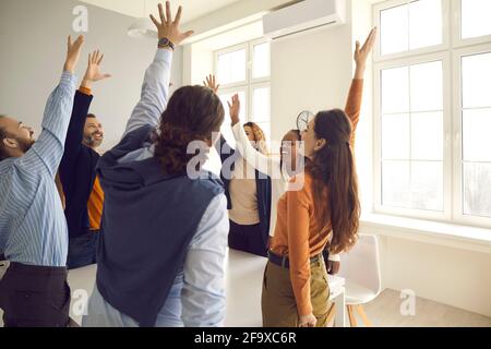 Team of happy diverse employees raising hands voting for good suggestion in corporate meeting Stock Photo