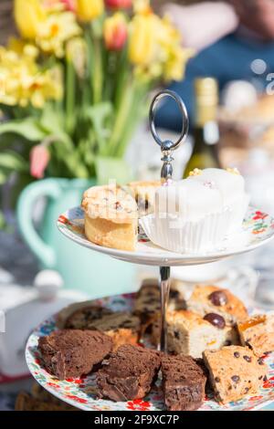 English afternoon tea with cake and sandwiches on a tiered cake stand in a floral garden on a beautiful sunny day Stock Photo