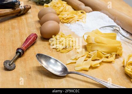 Making homemade pasta. Sliced rolled dough for pasta and prepared long pasta on wooden board with flour and eggs Rustic style Stock Photo
