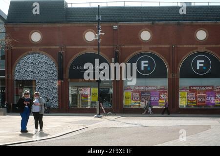 Store Closing sign in Debenhams window with shoppers wearing masks in the street outside. Preston, Lancashire, UK. Stock Photo