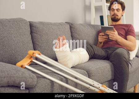 Young man sitting on sofa with broken leg in cast Stock Photo