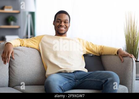 Happy black man sitting on sofa at home Stock Photo