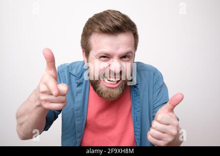 Strange bearded man makes a gesture with hands like it a gun and bares teeth. White background. Stock Photo