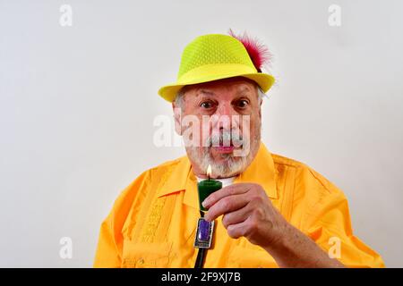 Senior male in a yellow outfit holding a candle in front of a white wall Stock Photo