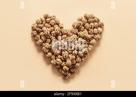 Fresh walnuts without shells in shape of heart on beige background. Walnuts concept as healthy food for heart. Stock Photo