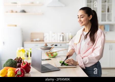 Woman cooking salad and using laptop and kitchen Stock Photo