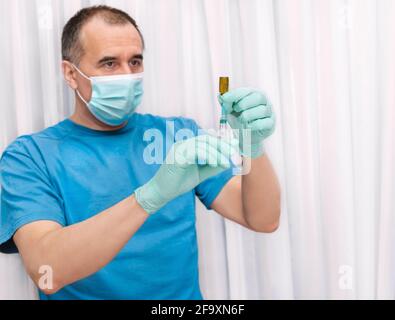 medical syringe with a bottle in male hands on a blurred background of a man in a mask Stock Photo