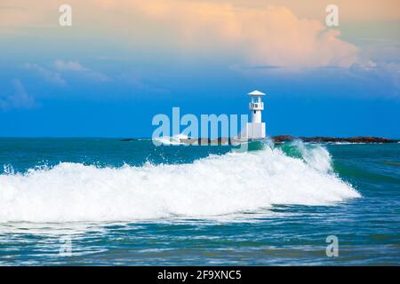 Rushing ocean waves and the white light house on a coastline in Khao Lak, Andaman Sea, Thailand, fantastic clouds against blue sky on summer dusk. Stock Photo