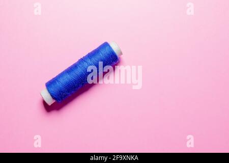 Sewing machine thread reel of blue color on pink background with selective focus. Stock Photo