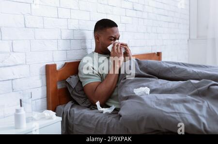 Sick Man Blowing Nose In Tissue Lying In Bed Indoor Stock Photo