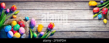Easter - Decorated Eggs In Nest With Colorful Tulips On Wooden Plank Stock Photo