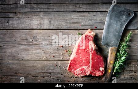 T-bone beef steak - Raw meat for grill with fresh herbs and cleaver Stock Photo