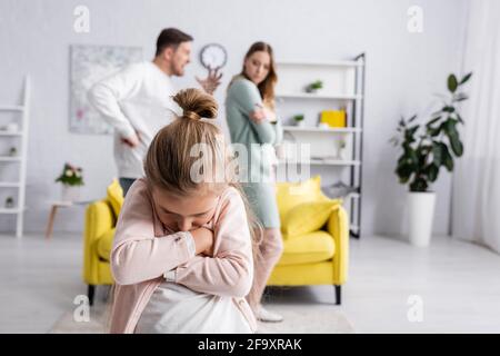 Displeased kid with crossed arms standing near father quarreling with mother Stock Photo