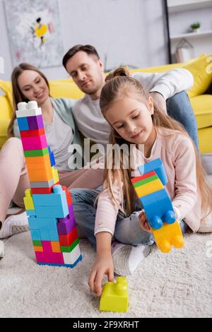 Kid stacking building blocks near parents in living room Stock Photo