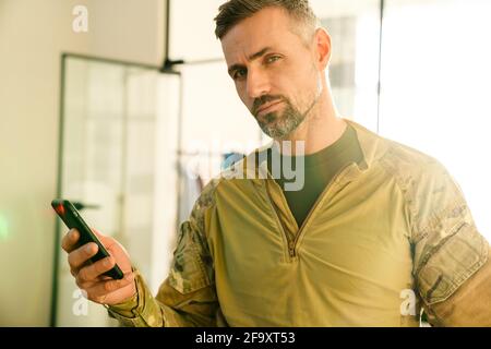 Confident masculine military man using mobile phone indoors Stock Photo