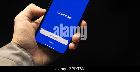 Kharkov, Ukraine - April 20, 2021: Man uses Coinbase app for buying bitcoin and cryptocurrency on the Apple iPhone, banner, black backrgound photo Stock Photo