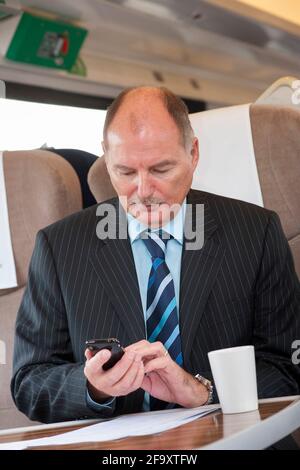 Business man using a mobile phone whilst travelling on a train in the UK. Stock Photo