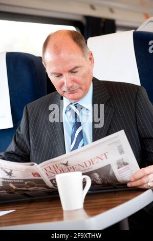 Business man reading a newspaper whilst travelling on a train in the UK. Stock Photo