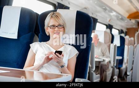 Business woman using a mobile phone whilst travelling on a train in the UK. Stock Photo