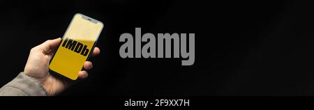 Kharkov, Ukraine - April 20, 2021: iMDB app logo banner with black background, copy space photo, man uses smartphone with application Stock Photo