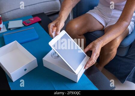 Older woman unboxing a new Apple ipad mini tablet in her living room. Stock Photo