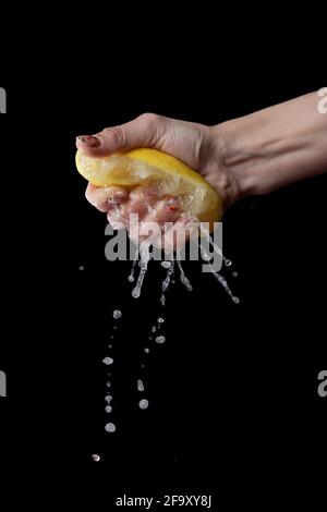 female hand squeezes juice from lemon on black background. Splashes and drops. Stock Photo
