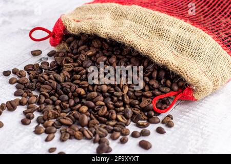 Fresh roasted brown organic arabica coffee beans in a burlap bag on light wooden background. Stock Photo