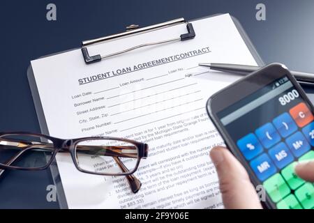 Blank Student Loan Application on table and hand holding a smartphone with calculator app. Education cost Stock Photo