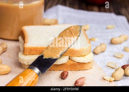 Homemade sandwich for breakfast with fresh crunchy peanut butter and bananas on light textile background. Stock Photo