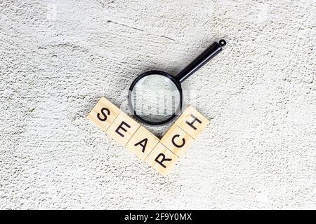 Black magnifying glass with search text on light gray background. Statistic analyzing and scientific research concept. Stock Photo