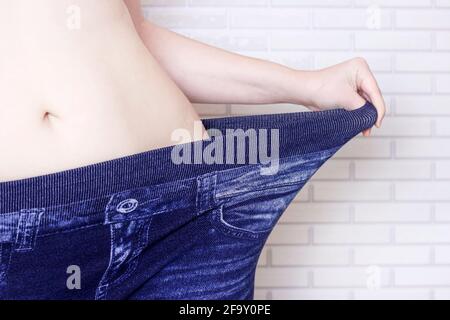 Young caucasian woman in blue oversized jeans pants. Success diets result, weight loss concept. Stock Photo