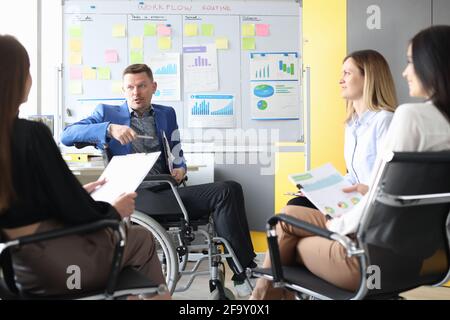 Business coach in wheelchair conducts business meeting of employees Stock Photo