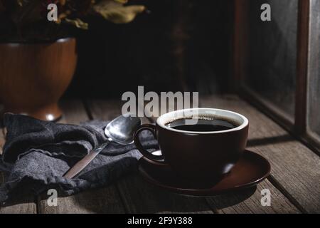 Cup of hot coffee next to a window on a rustic wooden table Stock Photo