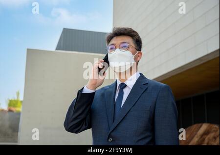 Middle-aged Asian businessman in the city wearing a mask and using a smartphone. Stock Photo