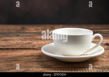 An empty white ceramic cup and saucer on a wooden brown background. Side view, copy space. Stock Photo