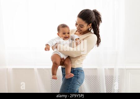 Joyful Black Mommy Carrying Baby In Arms Standing At Home Stock Photo