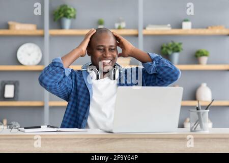 Business success and luck. Excited black businessman looking at laptop computer and touching head in excitement Stock Photo