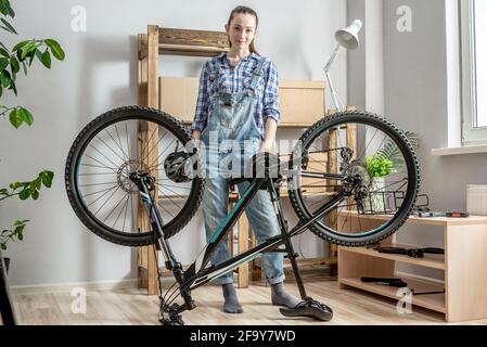Young female mechanic is standing next to a bicycle that is about to be disassembled for maintenance. Concept of repairing and preparing the bike for Stock Photo