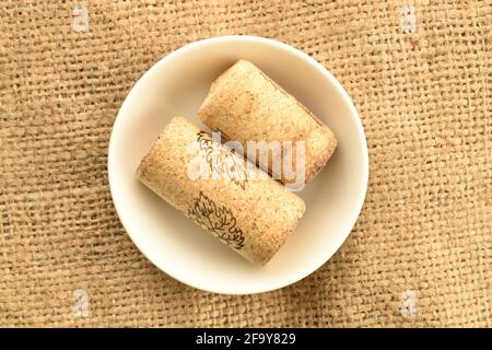 Two light brown wine corks in a white saucer on sackcloth, close-up, top view. Stock Photo